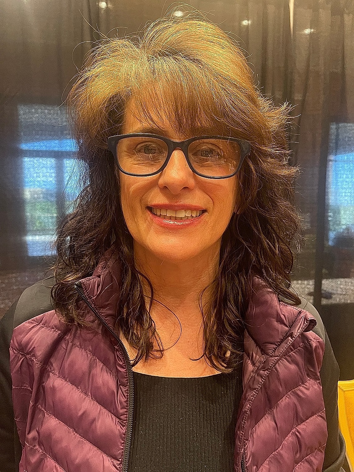 Smiling woman with glasses and curly hair.