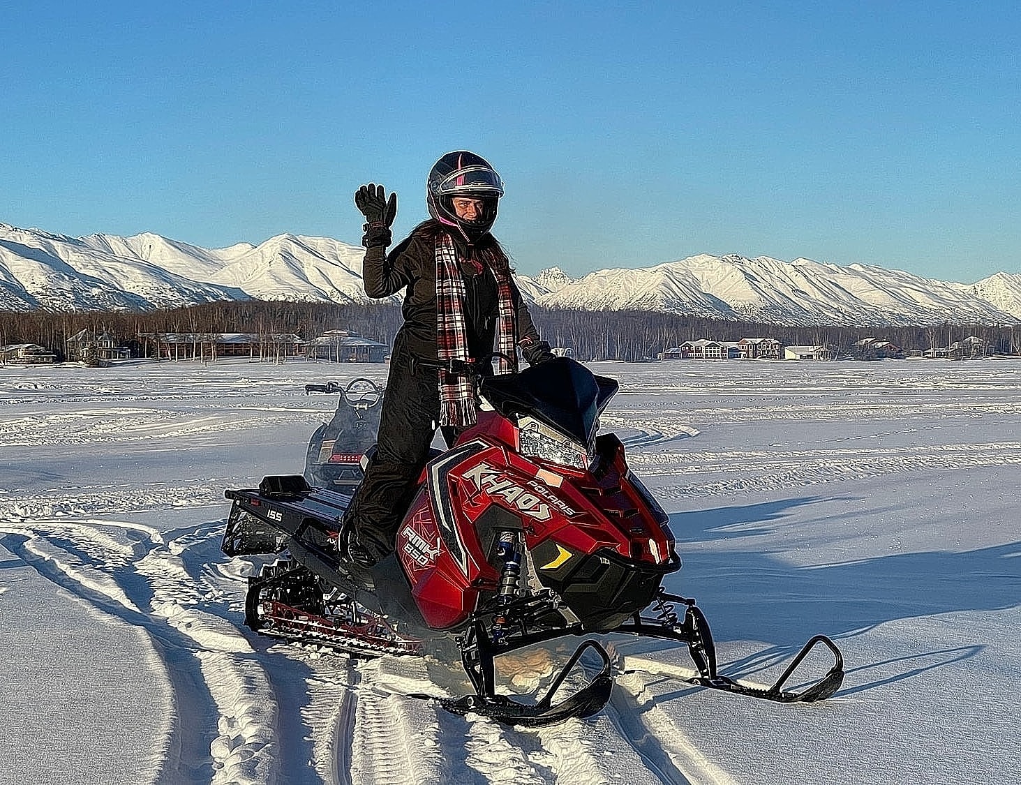 Person on snowmobile in snowy landscape, waving.