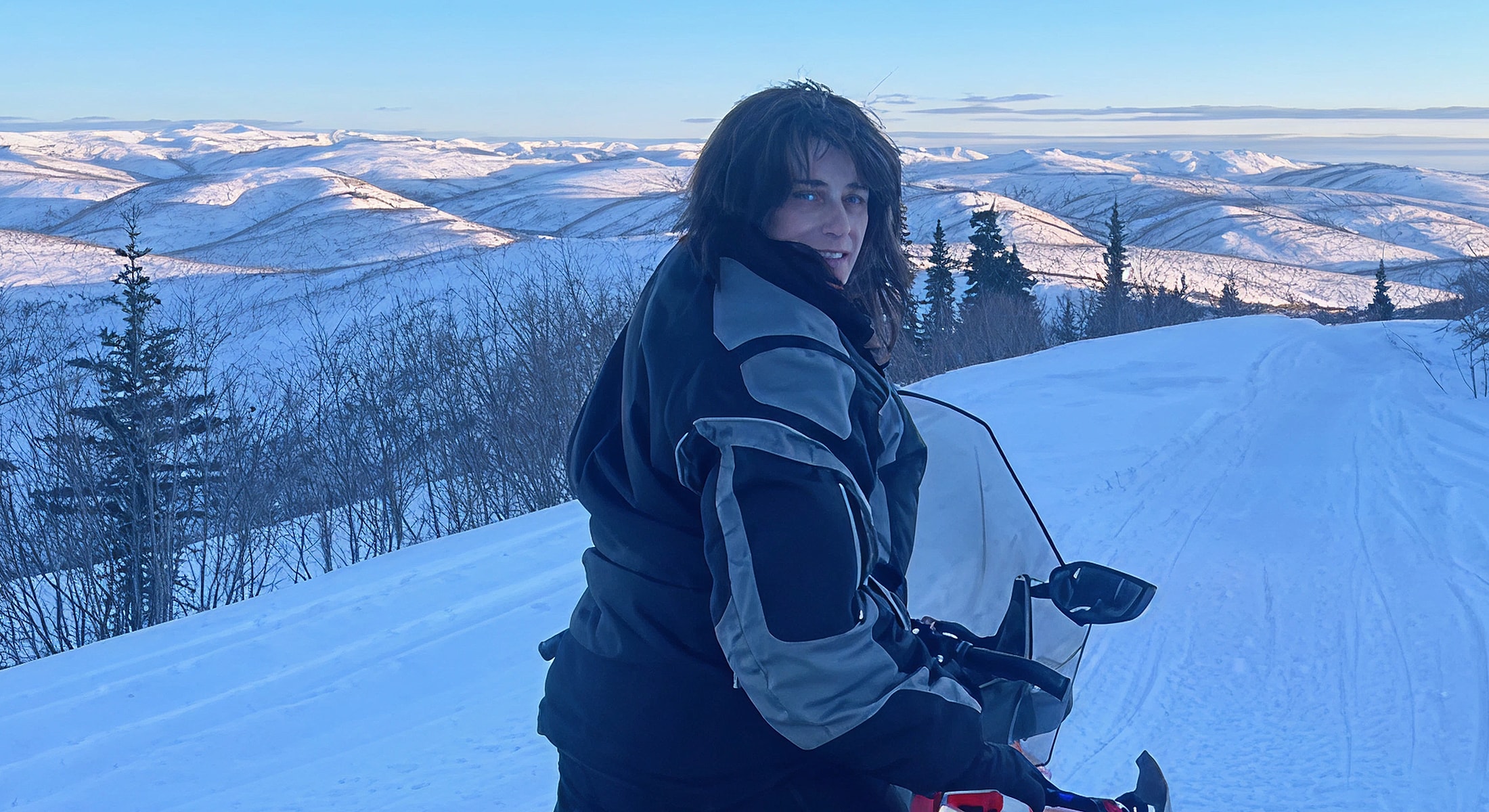Person on snowmobile in snowy mountainscape.