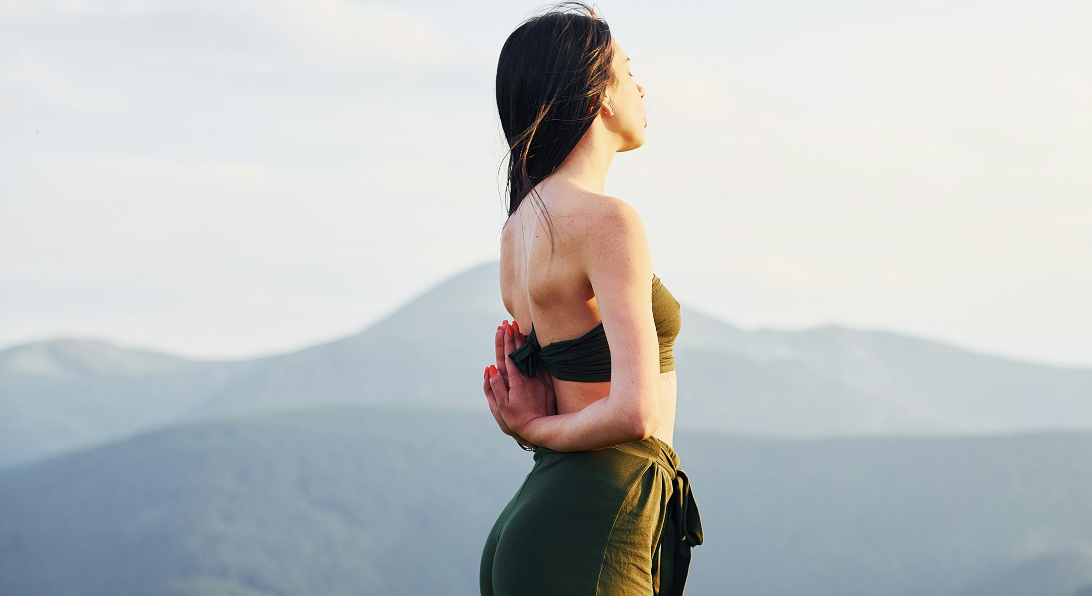 Woman practicing yoga outdoors against mountain backdrop.